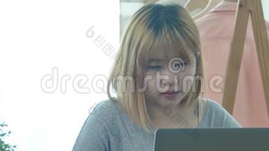 美丽的年轻微笑的女人，在笔记本电脑上工作，一边享受着温暖的咖啡，坐在家里的客厅里。